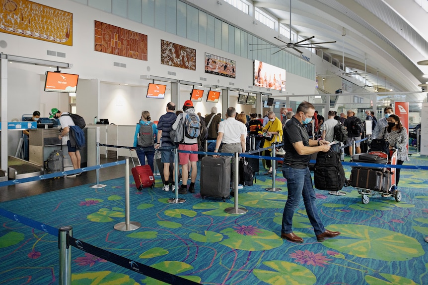 There is a long line of people wearing masks lined up at the check-in counter at the Darwin Airport 