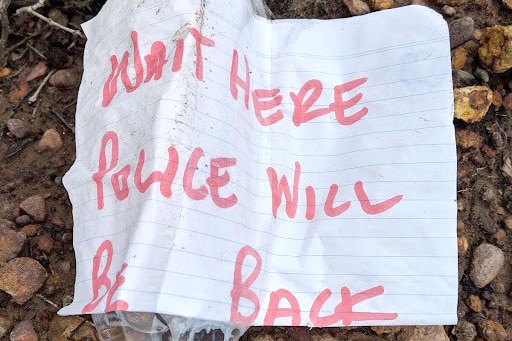 A message written on a piece of paper and taped to a plastic water bottle reads 'WAIT HERE POLICE WILL BE BACK'.