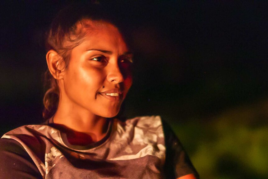 Indigenous teenager Zeritta Jessell's face is lit up by a campfire.