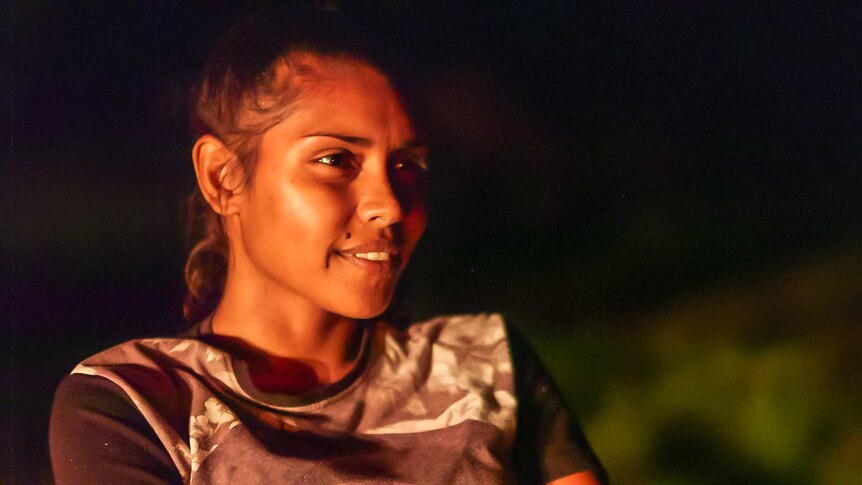 Indigenous teenager Zeritta Jessell's face is lit up by a campfire.