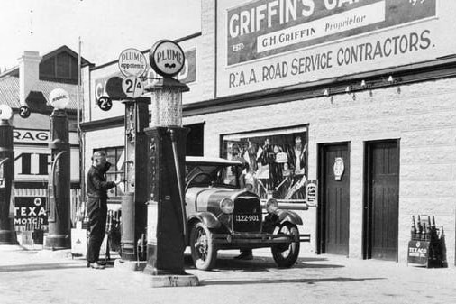 A black and white photo showing an attendant pumping petrol at a 1920s service station.