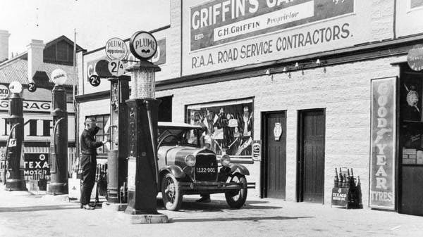 A black and white photo showing an attendant pumping petrol at a 1920s service station.