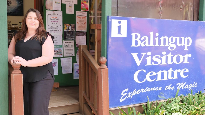 A woman stands next to a sign which reads Balingup visitor centre