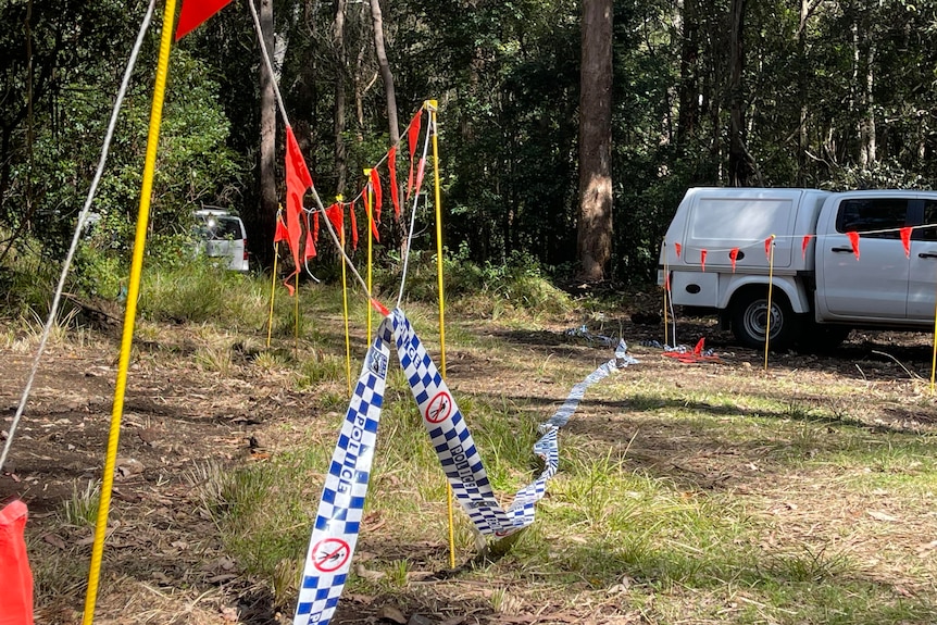 police tape loosely hung, two cars parked amongst bushland 