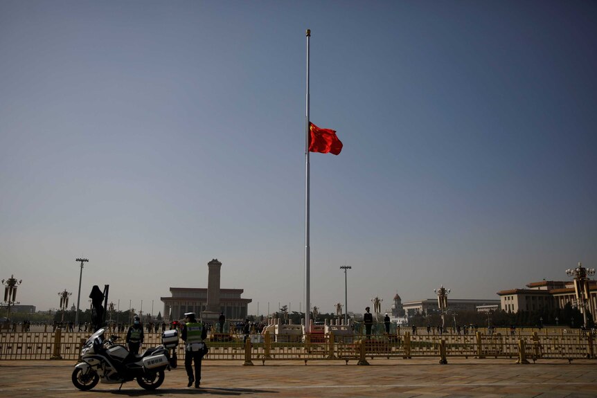 A red flag flaps in the breeze as it flies at half mast over an empty town square watched by a solitary police officer.