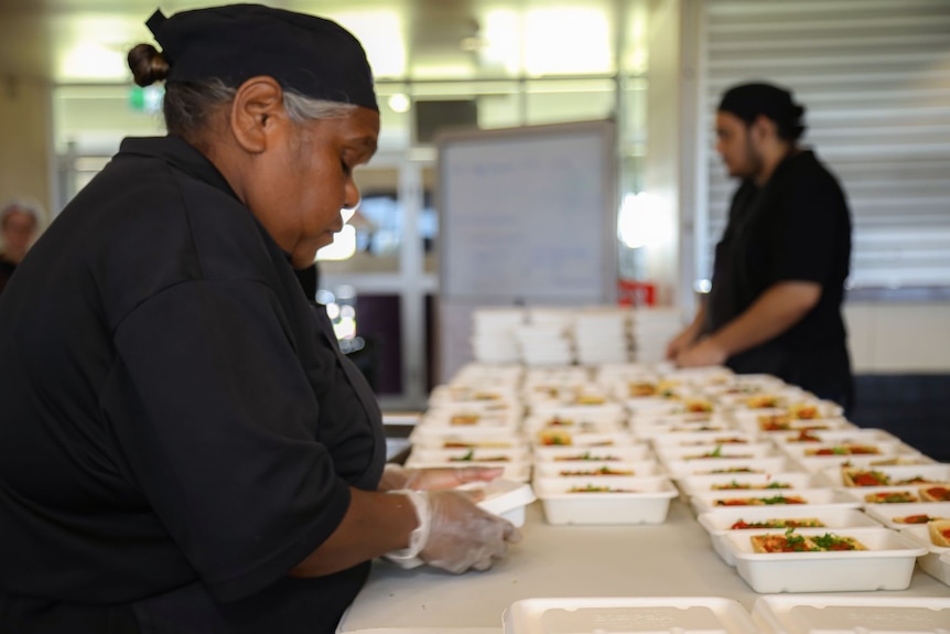 A woman in a chef's uniform seals a container of food.