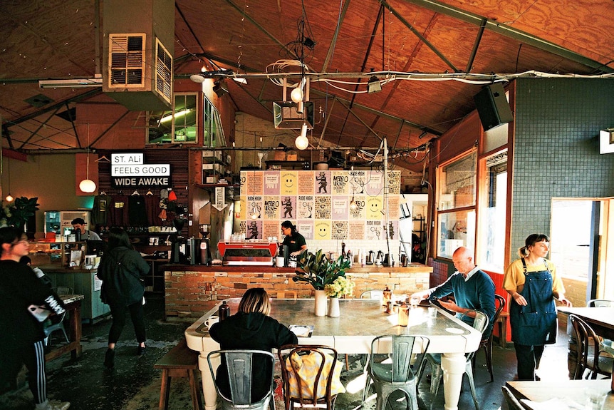 Customers sip coffee while waitstaff work at a Melbourne cafe