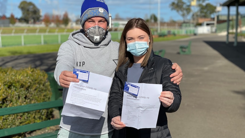 A couple holding up their vaccination paperwork