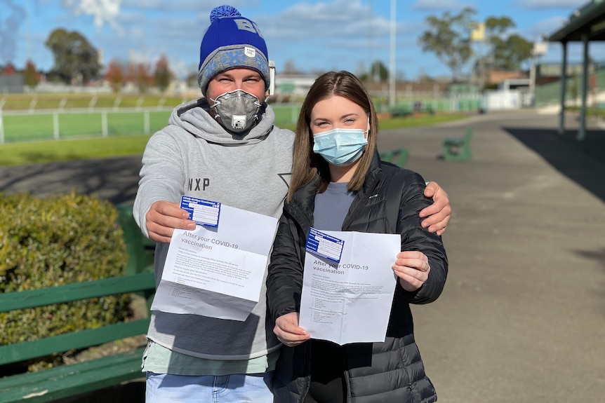 A couple holding up their vaccination paperwork