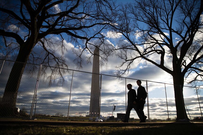 People pass a barricade in view of the Washington Monument as preparations continue ahead of the inauguration.