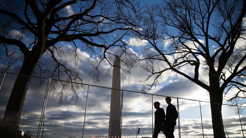 People pass a barricade in view of the Washington Monument as preparations continue ahead of the inauguration.