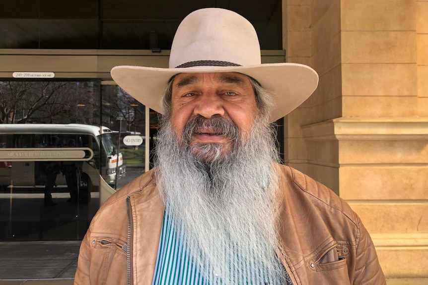 An older Indigenous man with a long, flowing beard, wearing a 10-gallon hat.