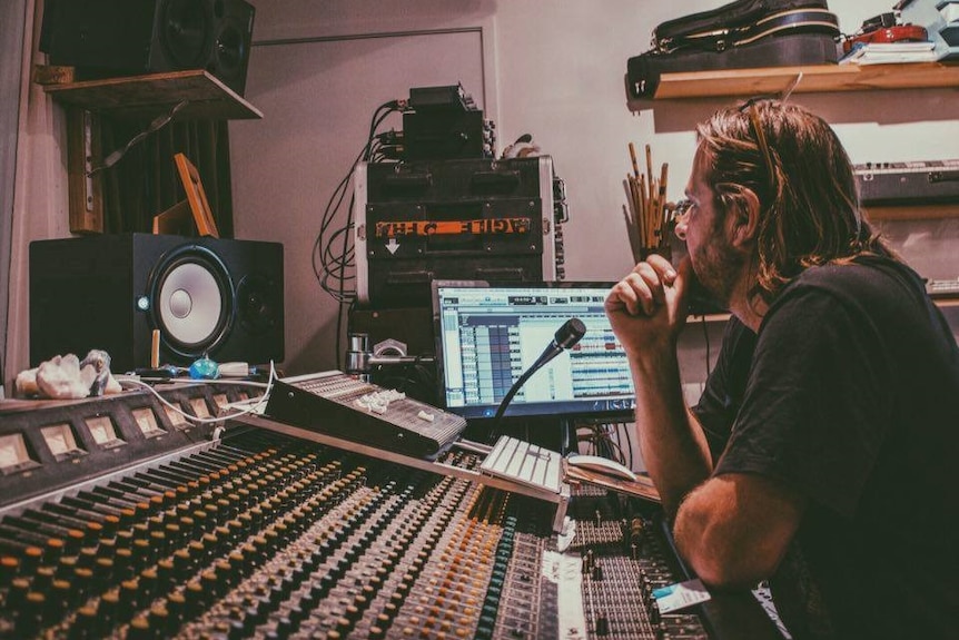 A man sits at a studio mixing desk