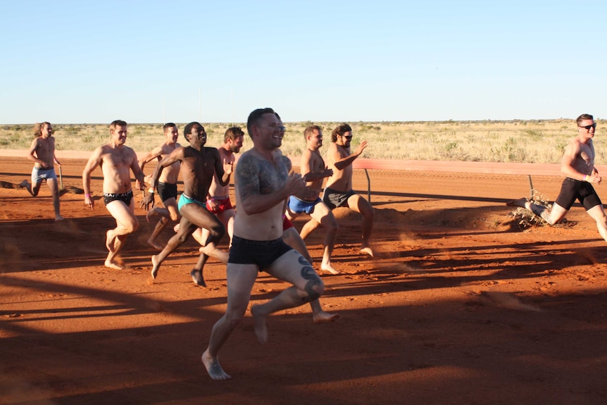 A group of men run along a dirt track dressed in their underwear.