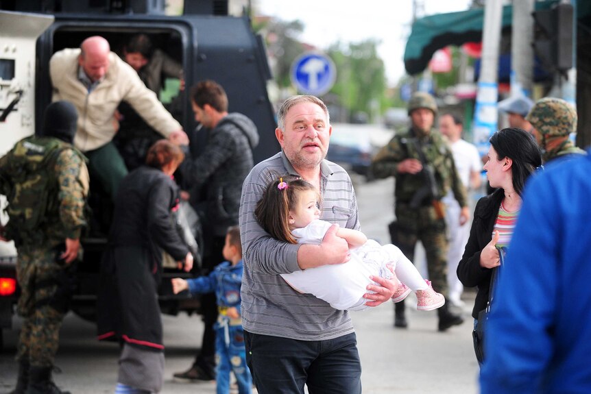 A man holding a child gets out of an armoured personnel carrier