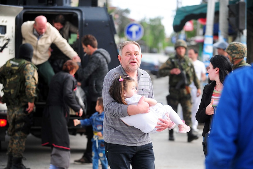A man holding a child gets out of an armoured personnel carrier