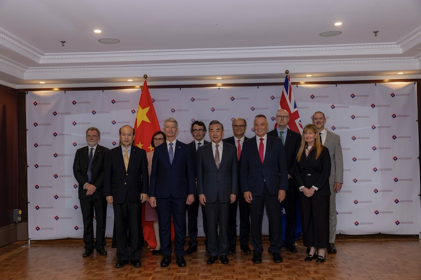 A group of political and business people stand in suits as they pose for a photo in front of Chinese and Australian flags.