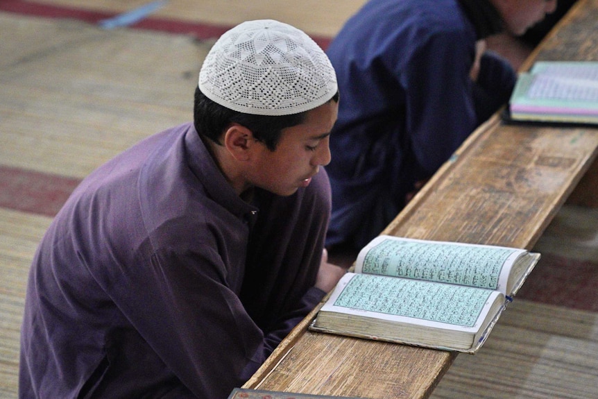 A boy crouched over a table looking at the Koran.