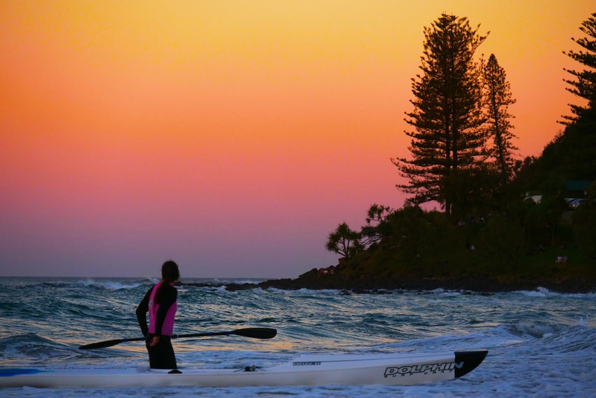 Sunrise over the ocean with paddle surfer in the foreground