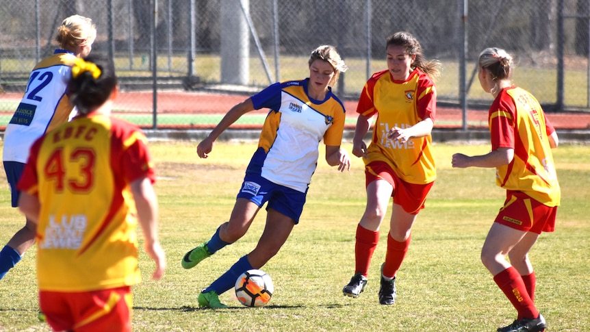 A player from Panania Diggers Soccer Club women's team changes direction with the ball at her feet, surrounded by defenders.