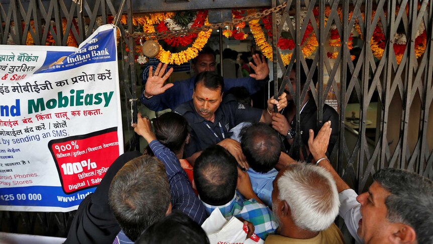 A security guard tries to close the gate as as people try to enter a bank in Mumbai.