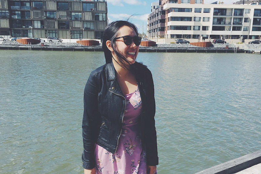 Carla Gee standing by the water while wearing sunnies and smiling