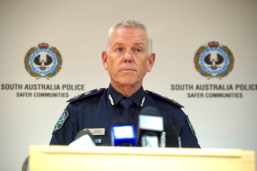 A man wearing a police uniform stands at a podium in front of SA Police logos