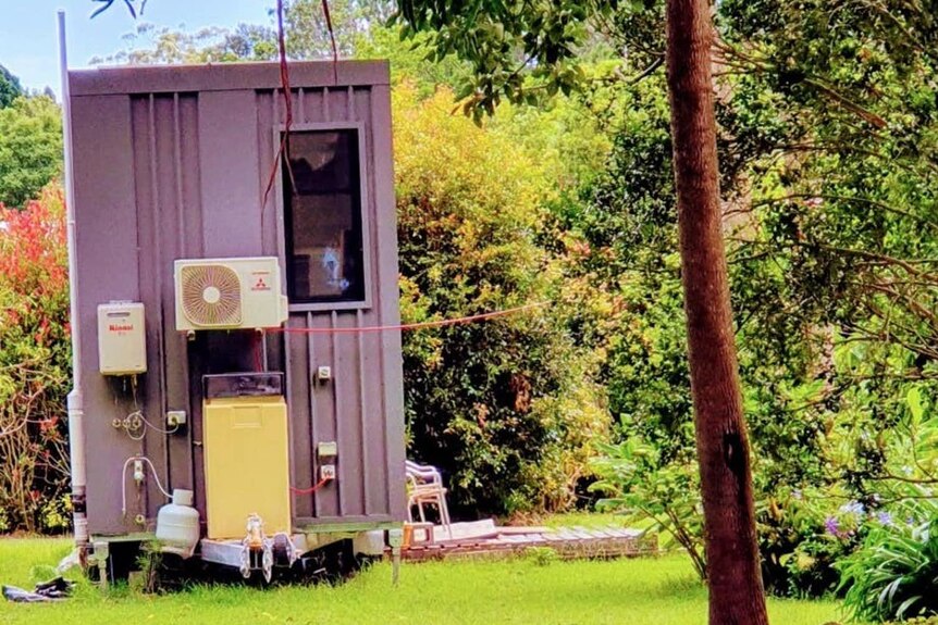 A small, purple house on a trailer base with air conditioning unit and gas cylinder affixed to one end.