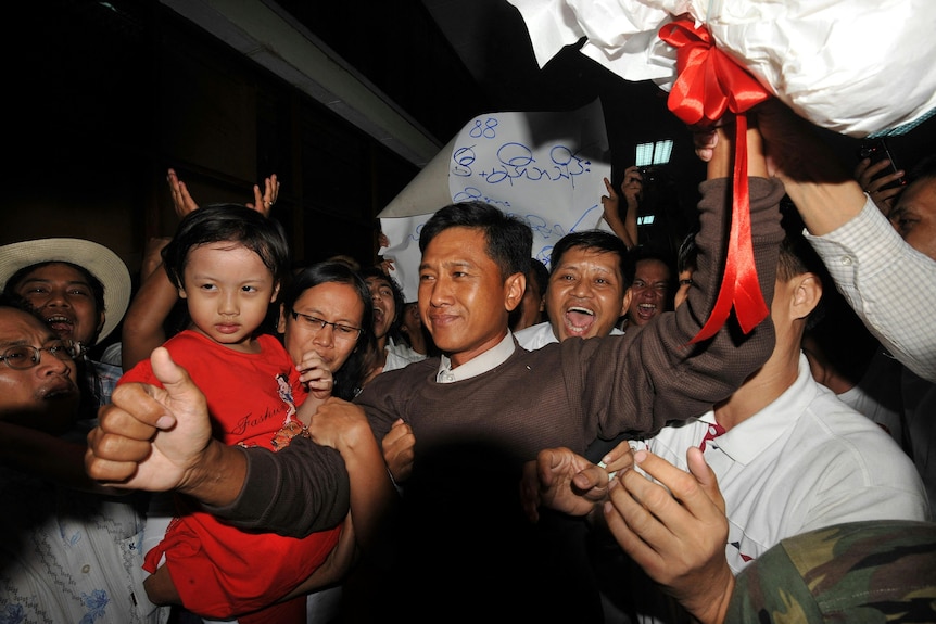 A man smiling surrounded by people.