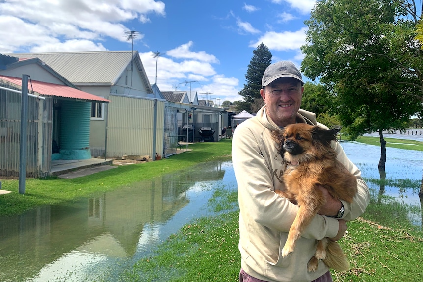 A man holding a dog outside shacks with water approaching them
