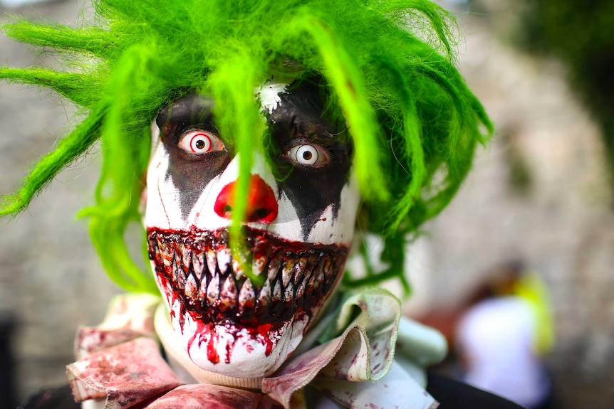 A man dressed as a scary clown with a green wig and bloody teeth.