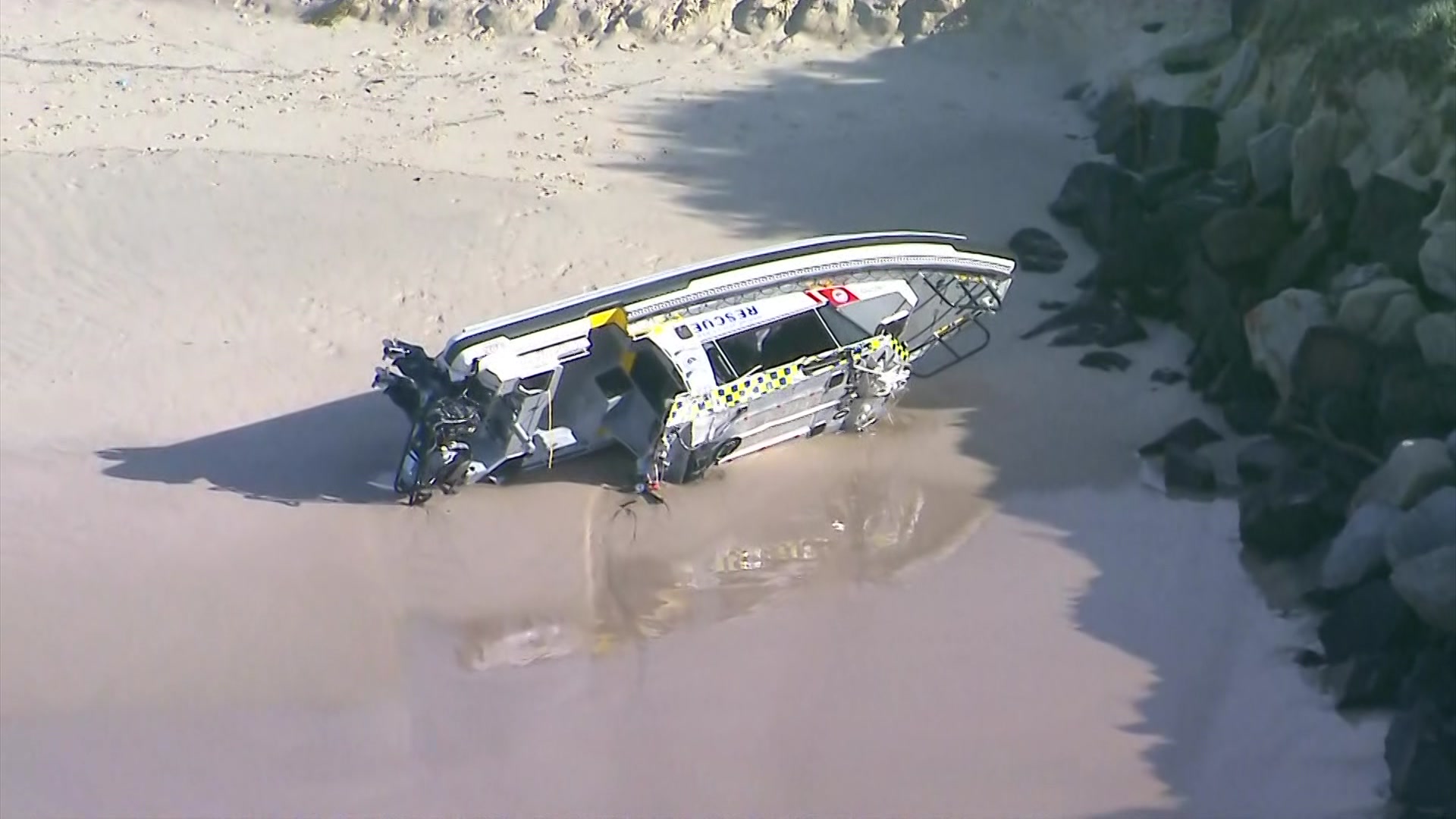 Marine Rescue boat washed ashore lying on its side near breakwall.