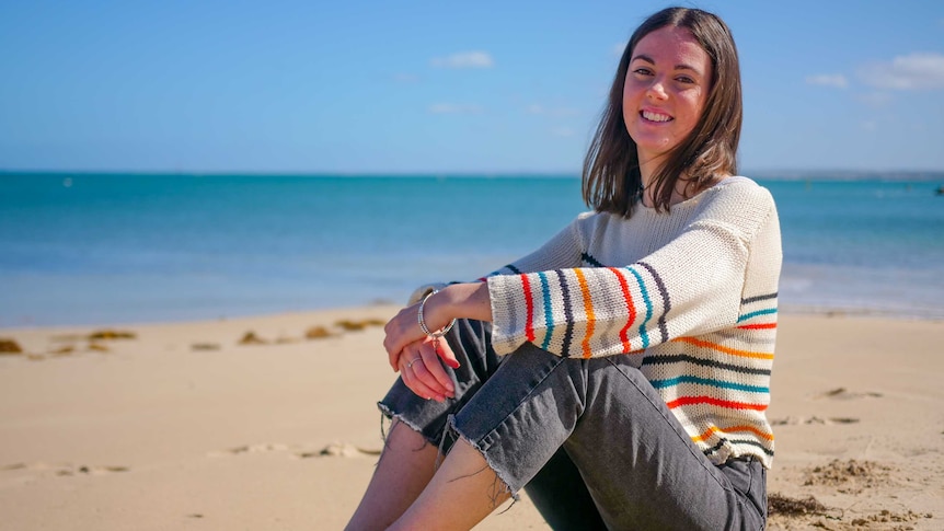 A young woman sits on the beach smiling