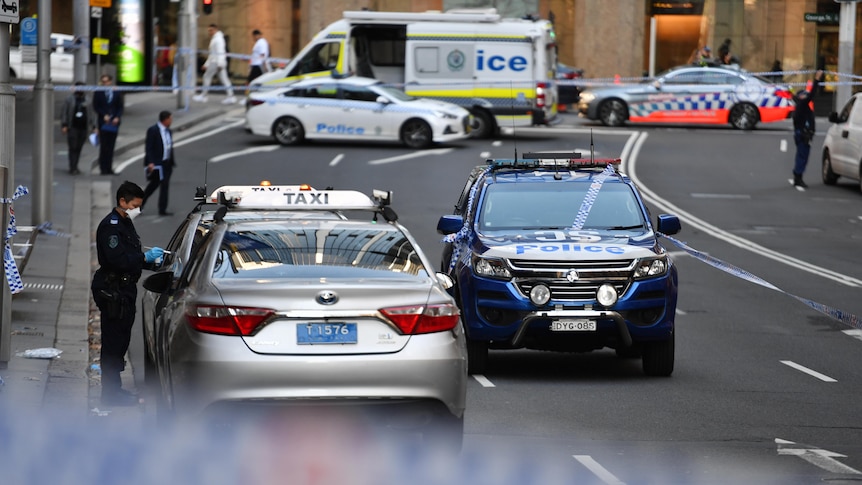 A police officer dusts for fingerprints as a large section of a Sydney CBD street is closed off with emergency vehicles.