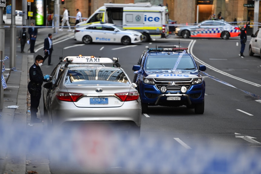 A police officer dusts for fingerprints as a large section of a Sydney CBD street is closed off with emergency vehicles.