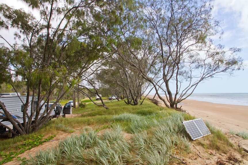 Caravans, vehicles and a solar panel are dotted along the sand dune beside the beach