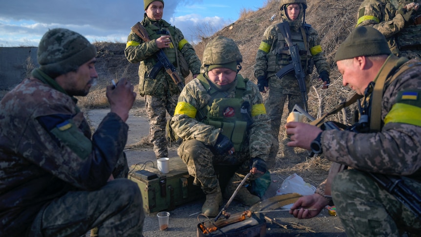 Ukrainian servicemen in military uniforms huddle around a small fire.