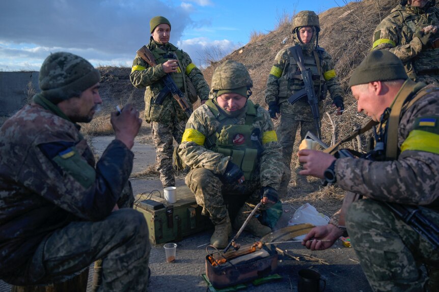 Ukrainian servicemen in military uniforms huddle around a small fire.