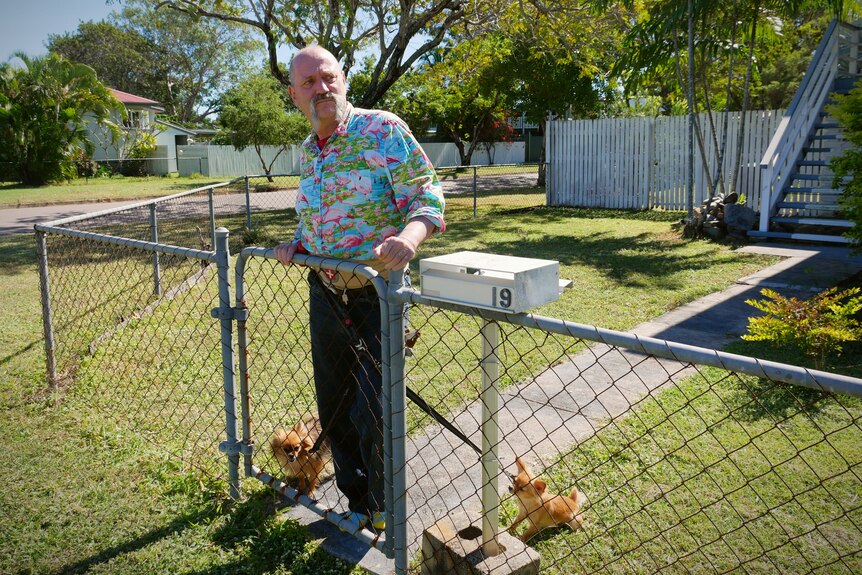 A man with two dogs on leashes stands at the front gate of a home