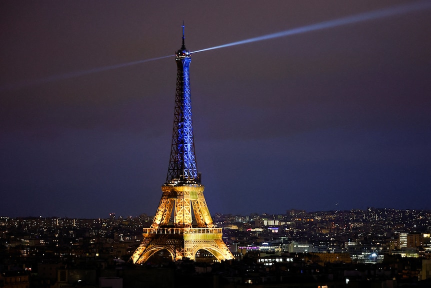 The eiffel tower at night, with one half lit blue and the other yellow in the colours of Ukraine. 