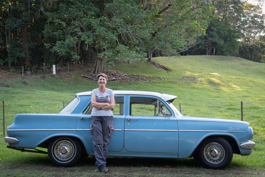 Portrait of Fiona Gray standing in front of her old blue Holden on a country road.