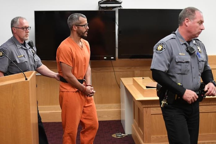 Accused Christopher Watts enters court in orange jumpsuit and handcuffs, flanked by two officers ahead of hearing.