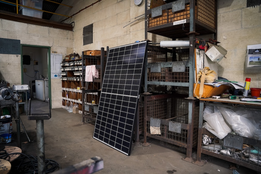 A large solar panel leans against shelving in a factory workshop.