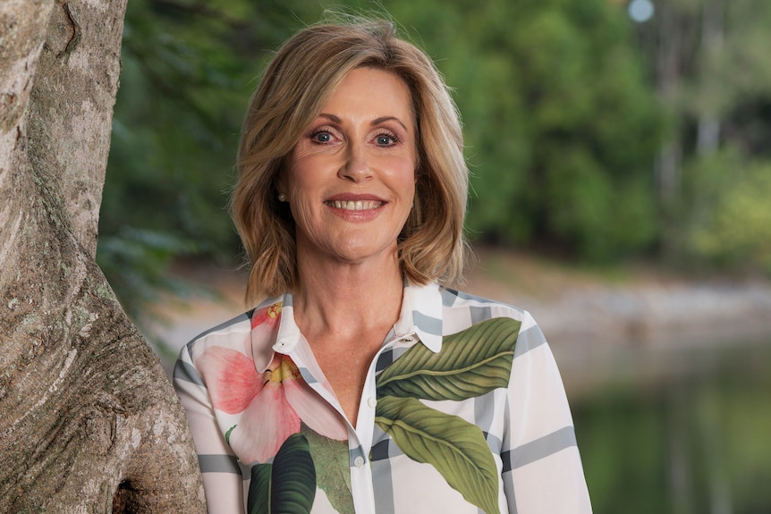 A woman smiles while leaning against a tree trunk.