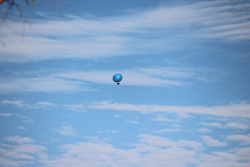 A blue balloon against a blue sky with soft wispy clouds.
