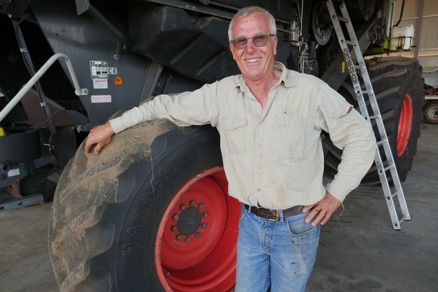 A middle aged man stands next to a tractor in a shed.
