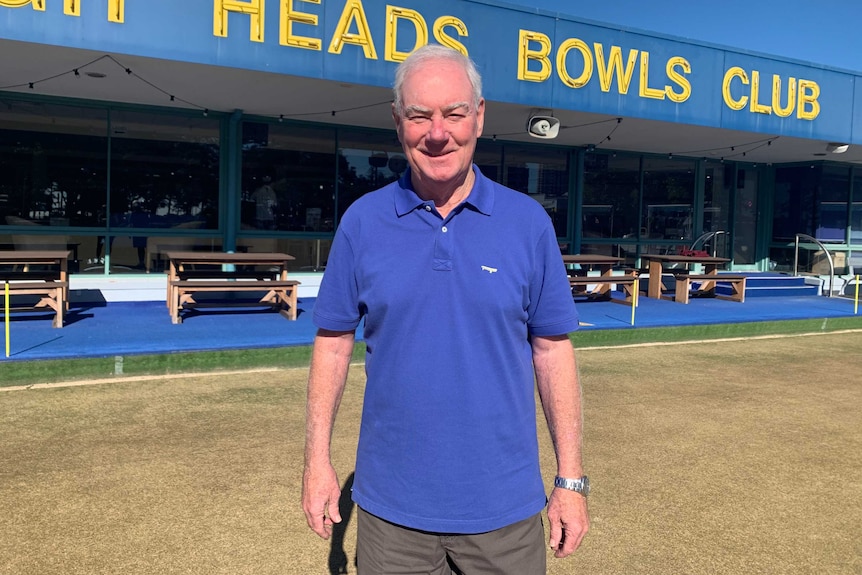 Burleigh Heads Bowls Club Chairman Paul Hynes standing on the green with clubhouse and sign behind him