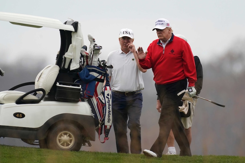 President Donald Trump waves as he plays golf.