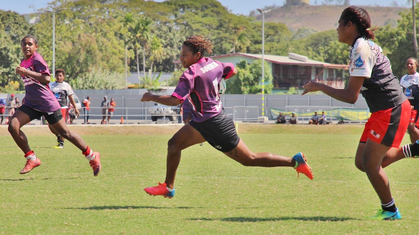 A woman with a ball tucked under her arm strides out on her way to scoring a try.