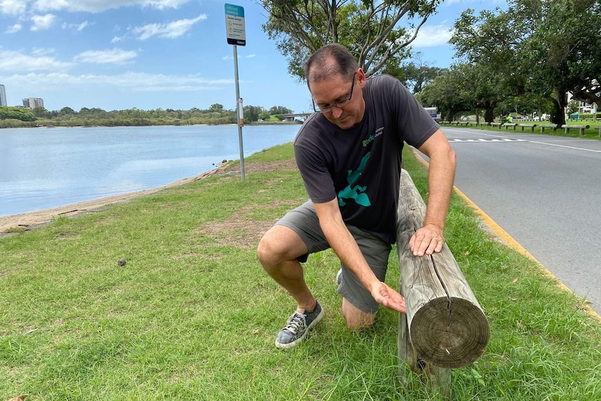 David Paynter kneels on ground using hand to show height of rising water level at a park.